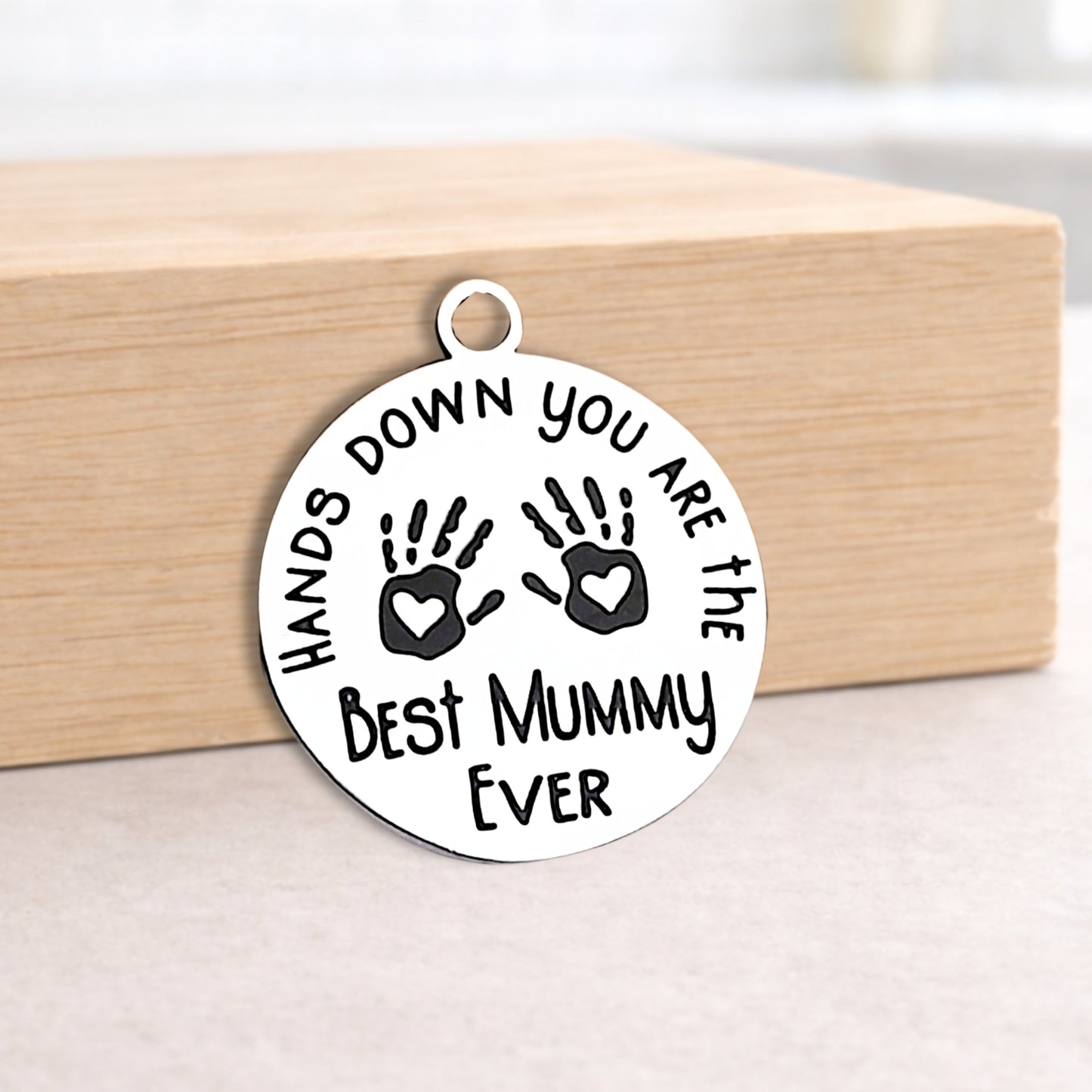 Round silver pendant with engraved text on a wooden block