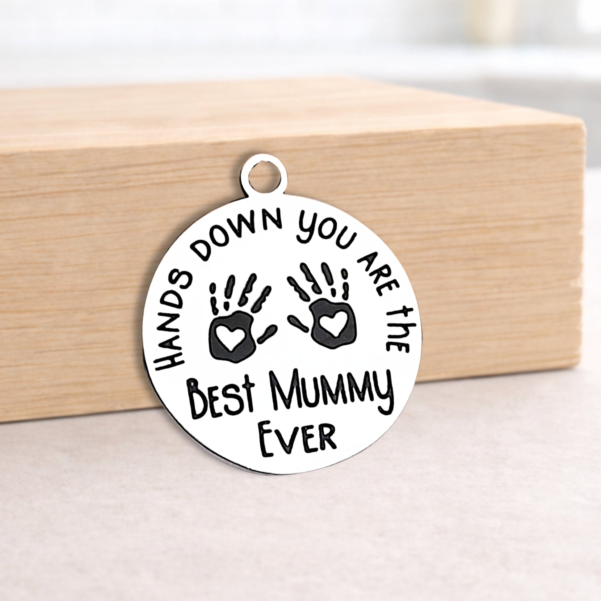 Round silver pendant with engraved text on a wooden block