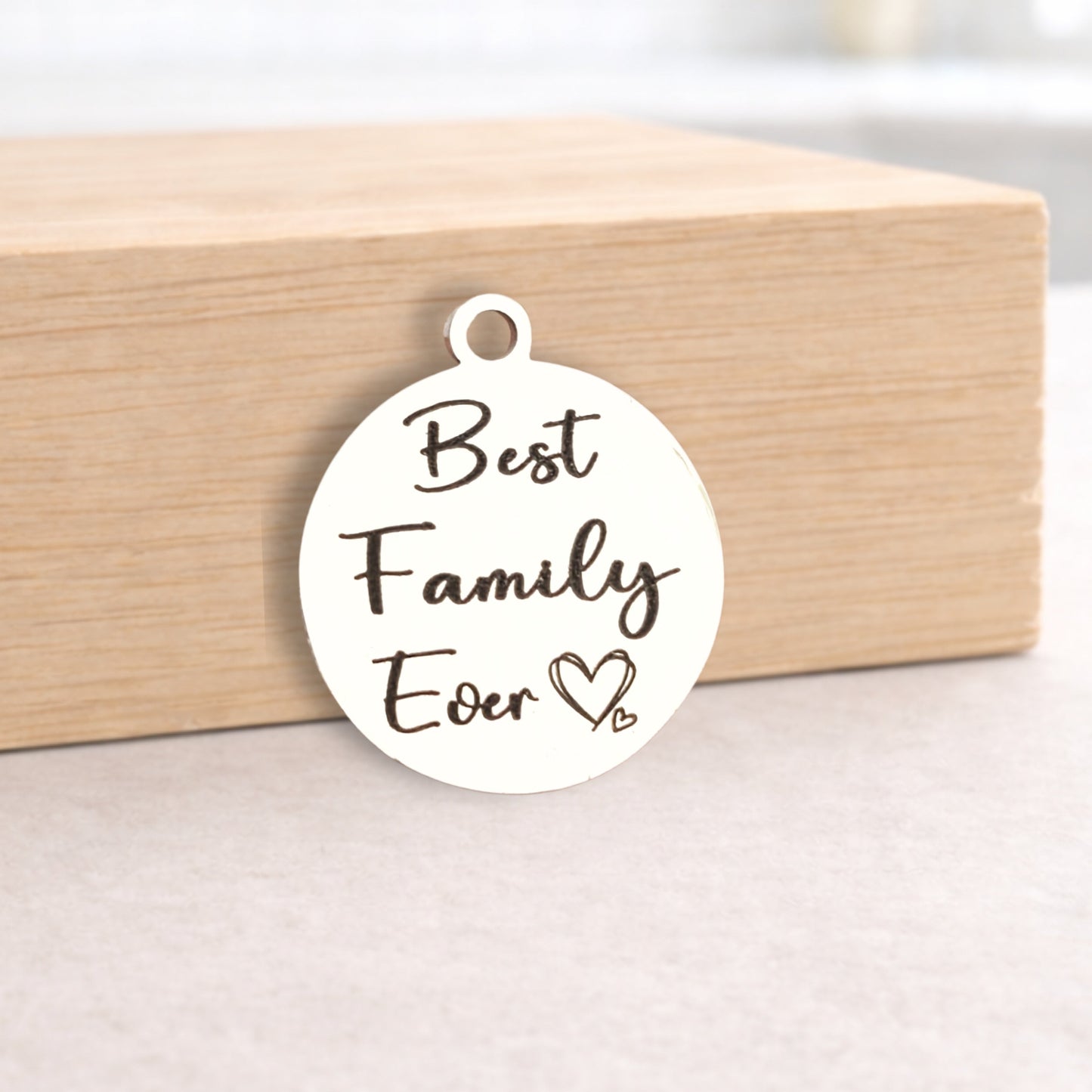 Round metal pendant with 'Best Family Ever' text on a wooden block