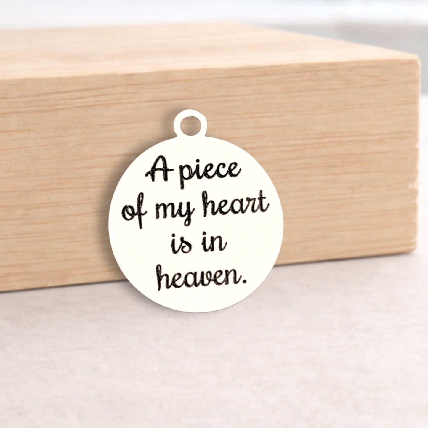 White pendant with 'A piece of my heart is in heaven' text on a wooden block.
