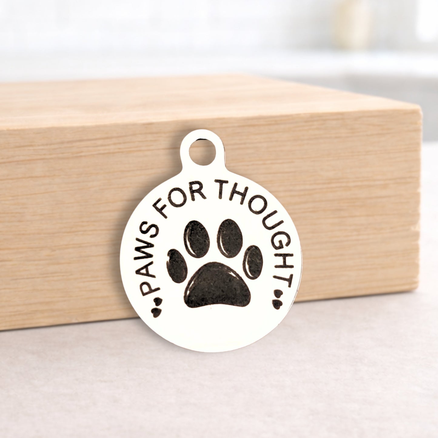 Metallic pendant with 'Paws for Thought' text and paw print design on a wooden block.