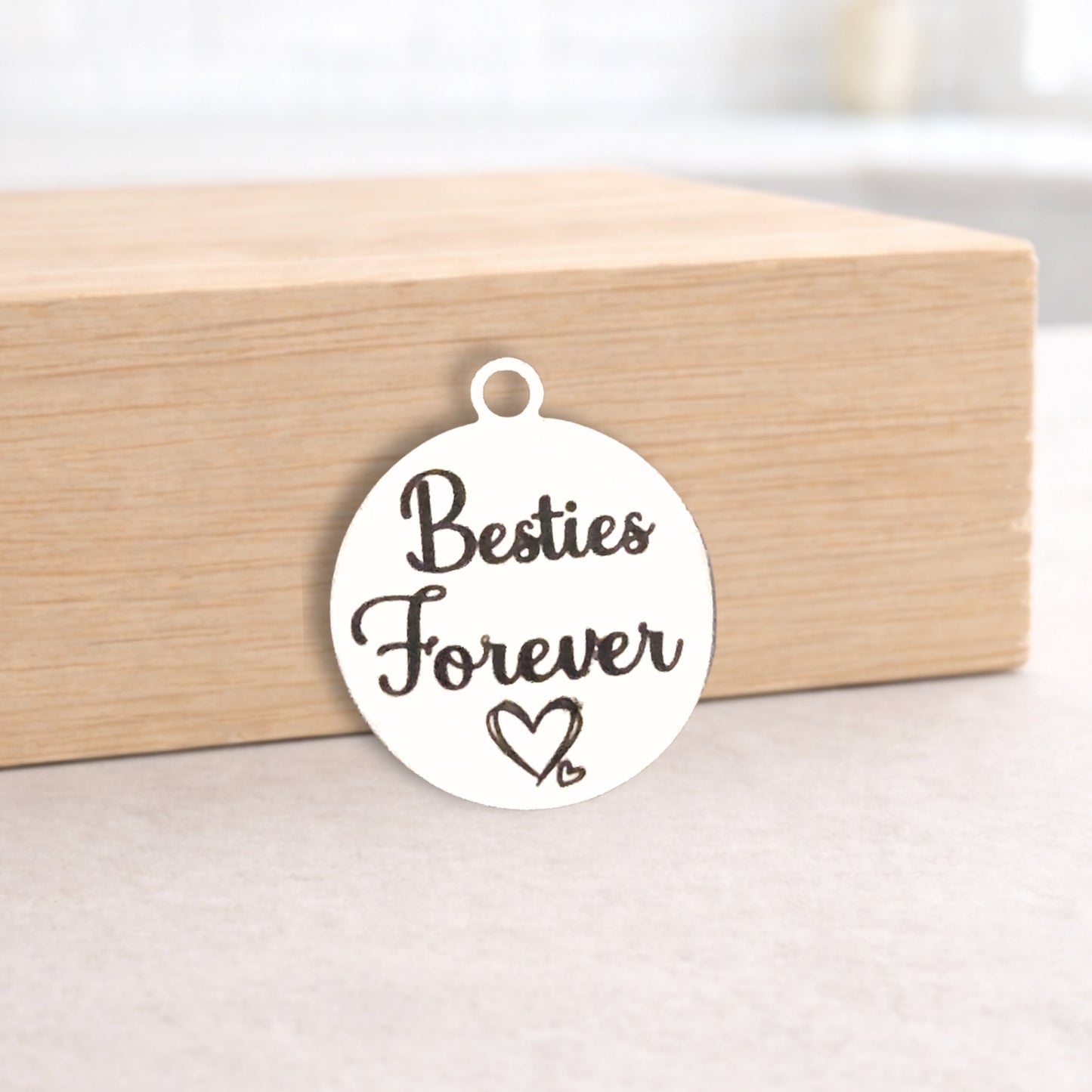 Round metal pendant with 'Besties Forever' text on a wooden block