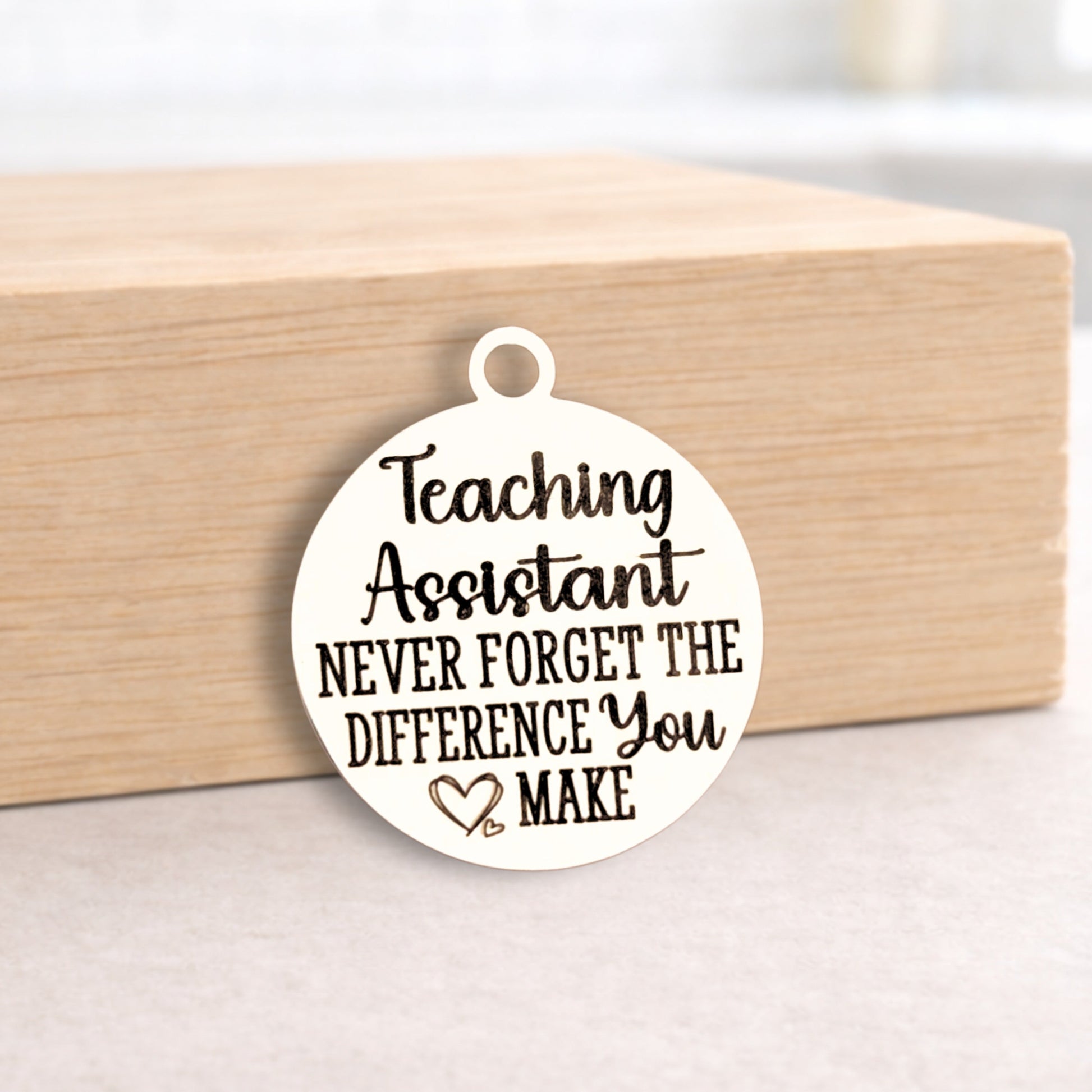 Round pendant with 'Teaching Assistant Never Forget the Difference You Make' text on a wooden block.