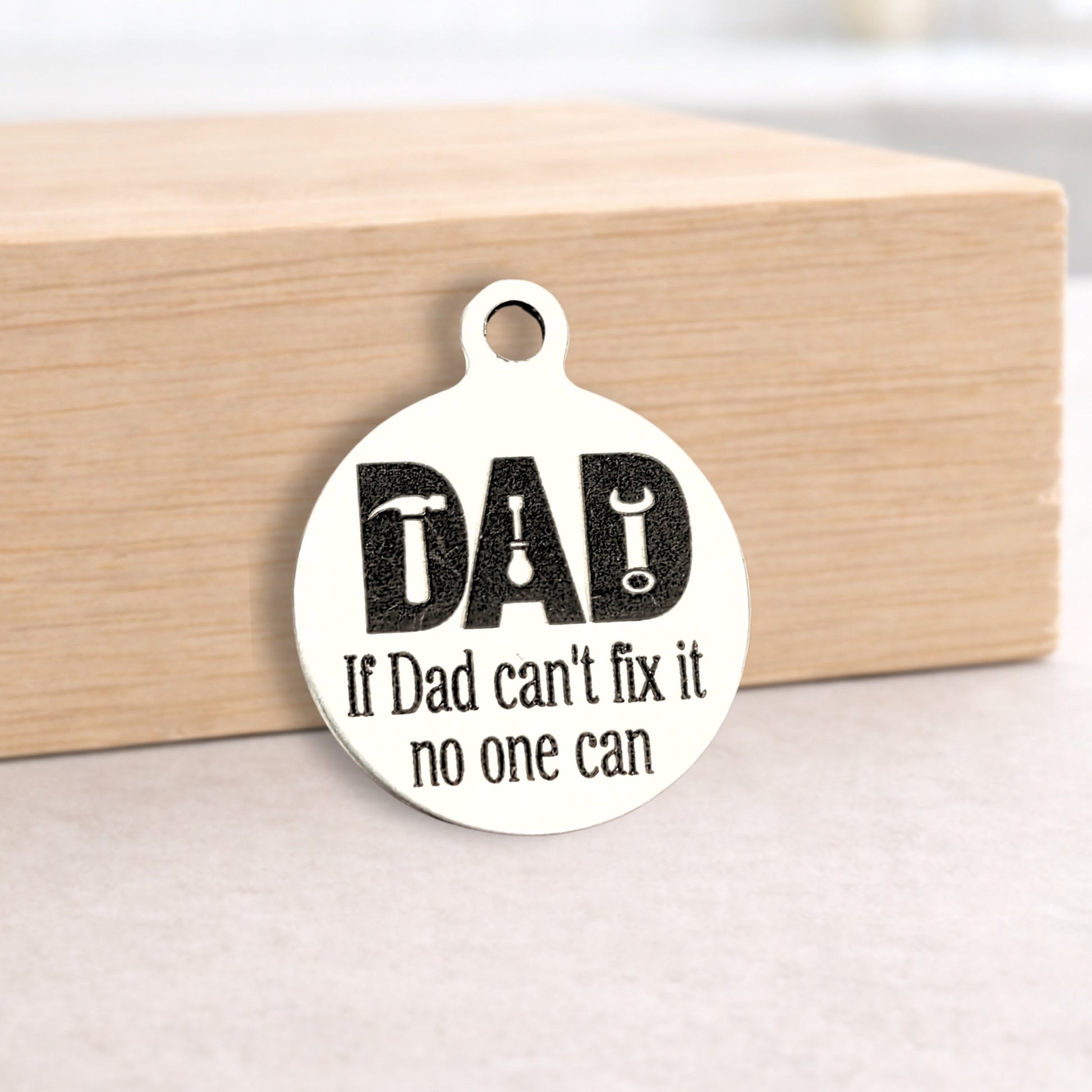 Round metal tag with 'DAD If Dad can't fix it no one can' text on a wooden block.