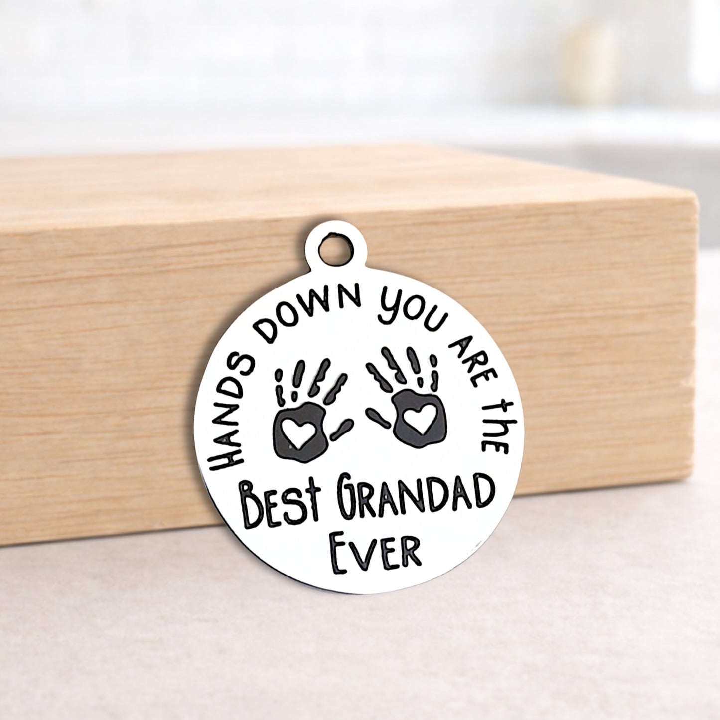 Round pendant with engraved text and handprints on a wooden block.