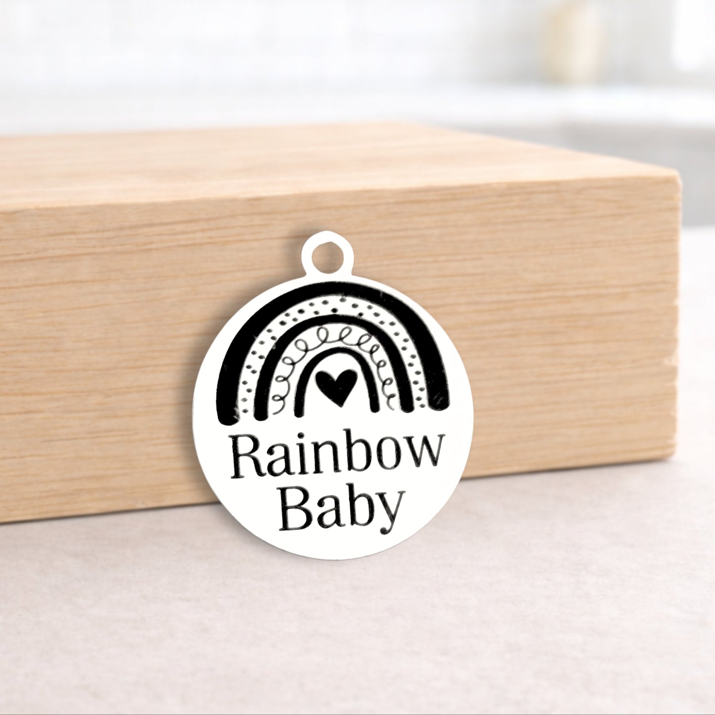 Round pendant with 'Rainbow Baby' text on a wooden block