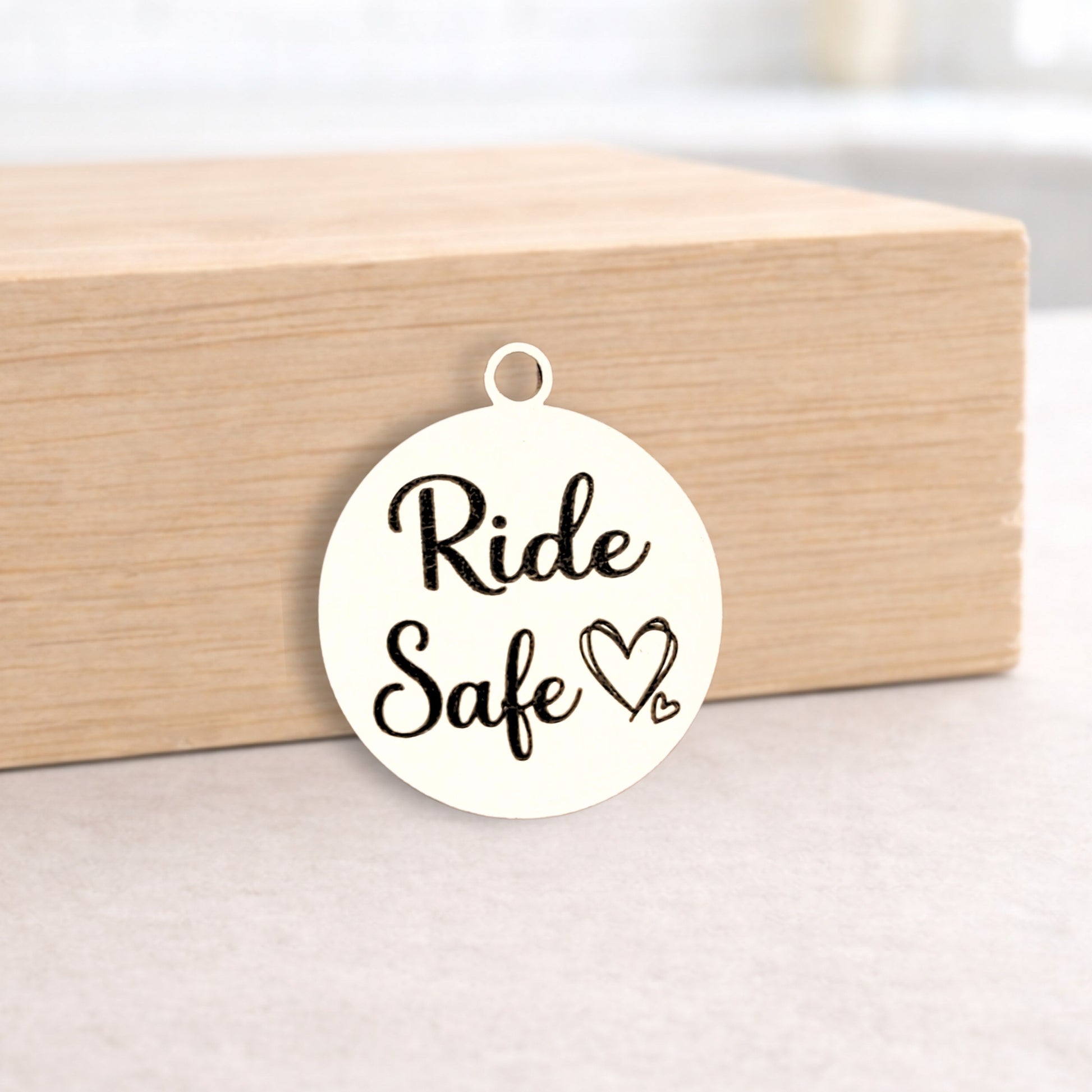 Round white pendant with 'Ride Safe' text on a light wooden block.