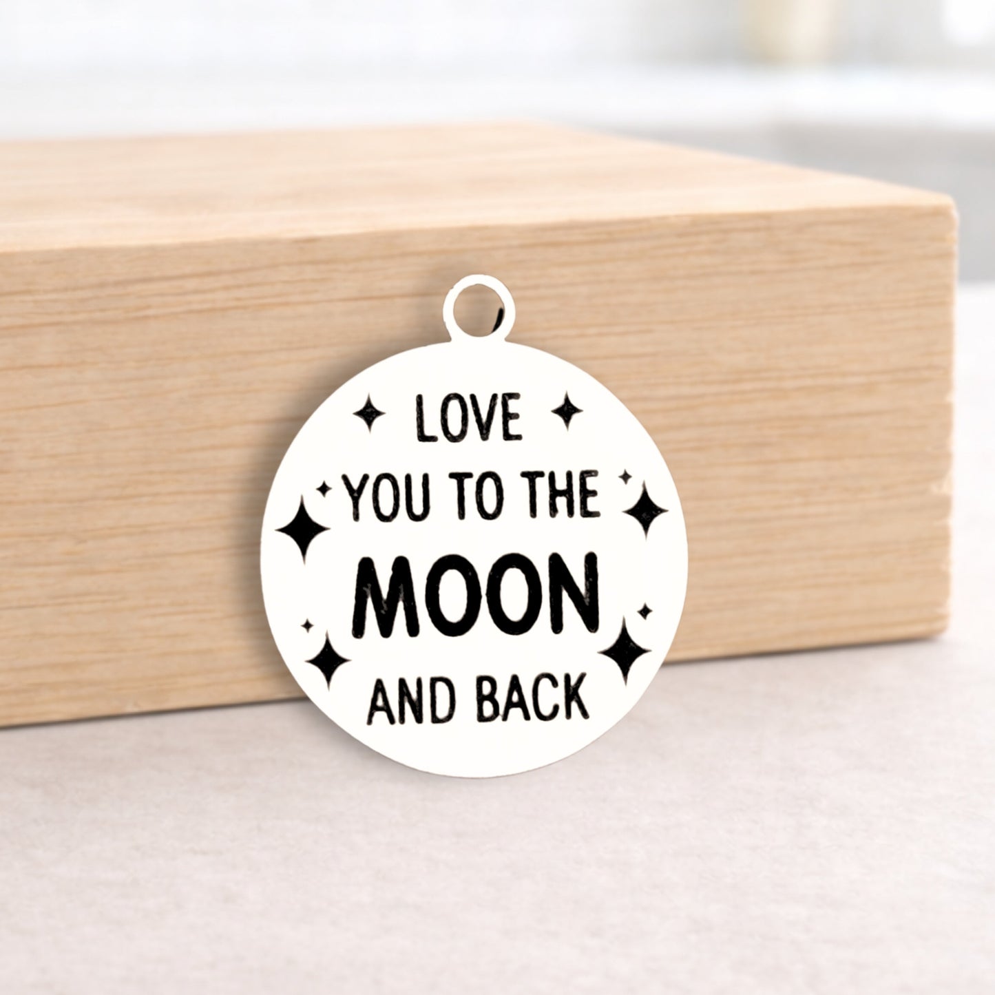 Circular pendant with 'Love you to the moon and back' text on a wooden block.
