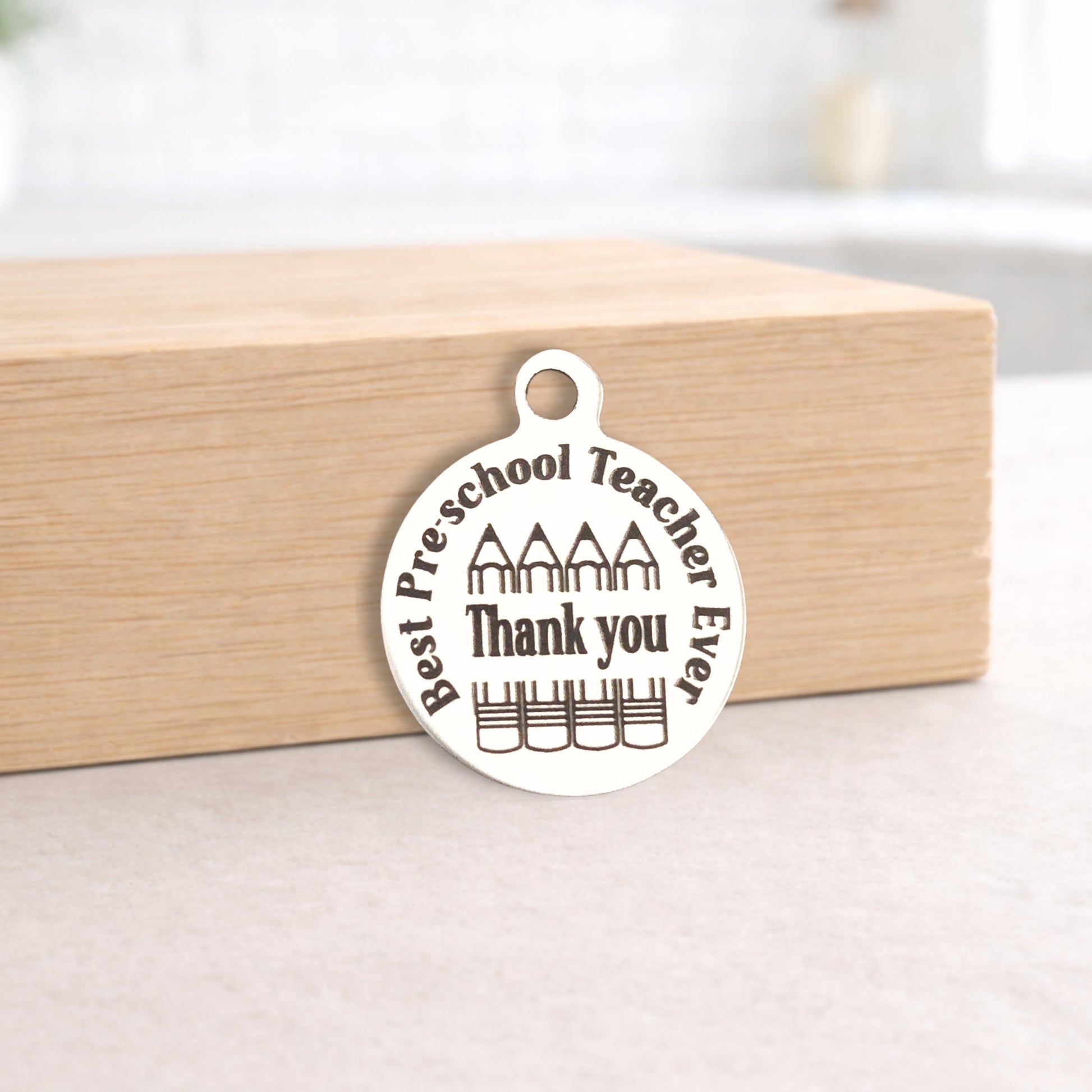 Metal pendant with 'Best Preschool Teacher Ever Thank you' text on a wooden block.