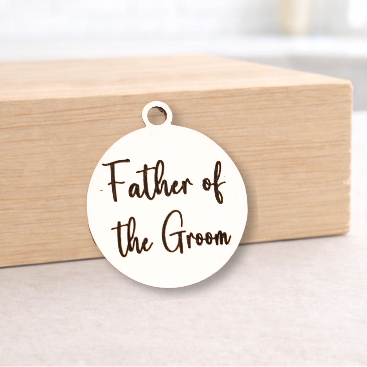 Round white pendant with 'Father of the Groom' text on a wooden block.