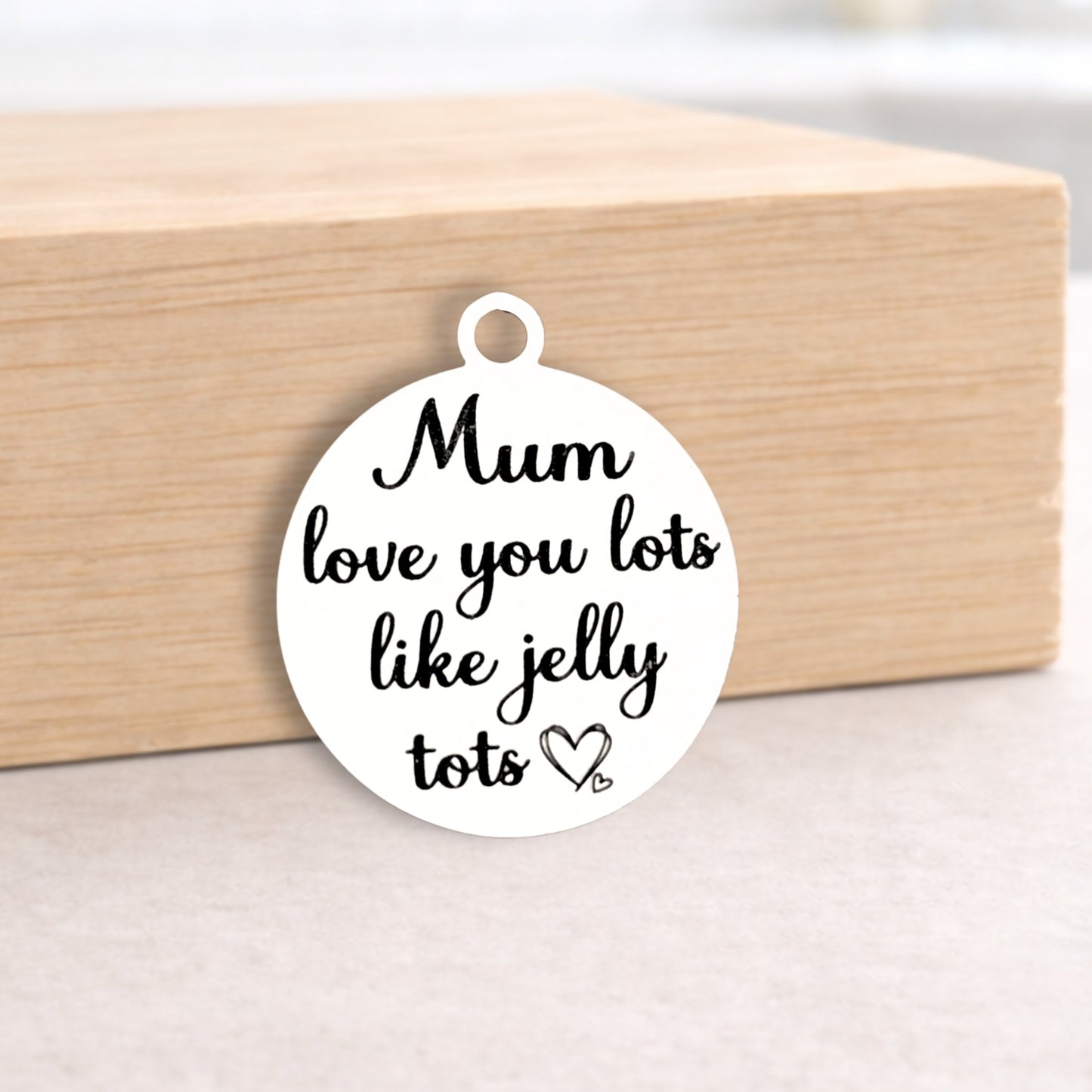 Round white pendant with black text 'Mum love you lots like jelly tots' on a wooden block.