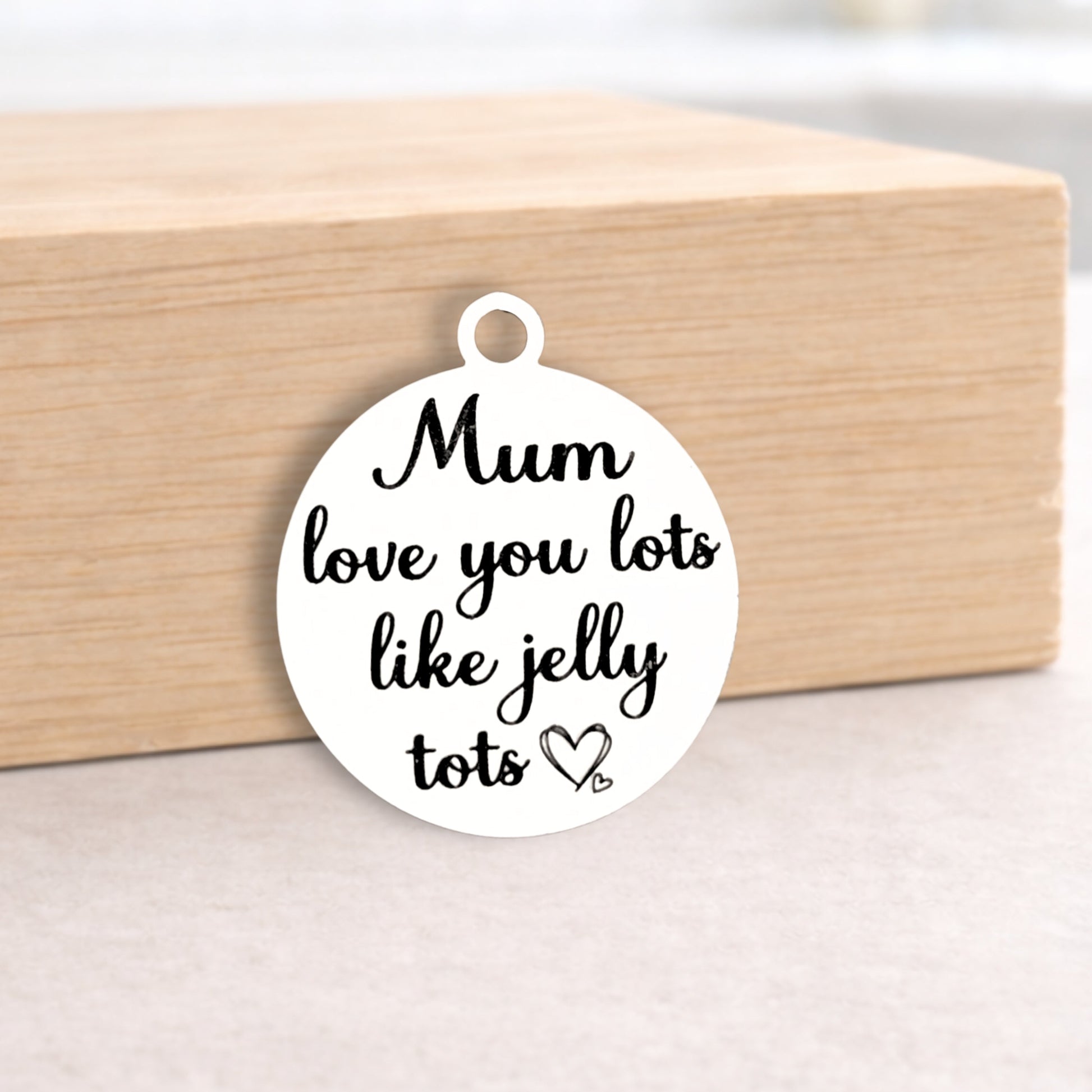 Round white pendant with black text 'Mum love you lots like jelly tots' on a wooden block.
