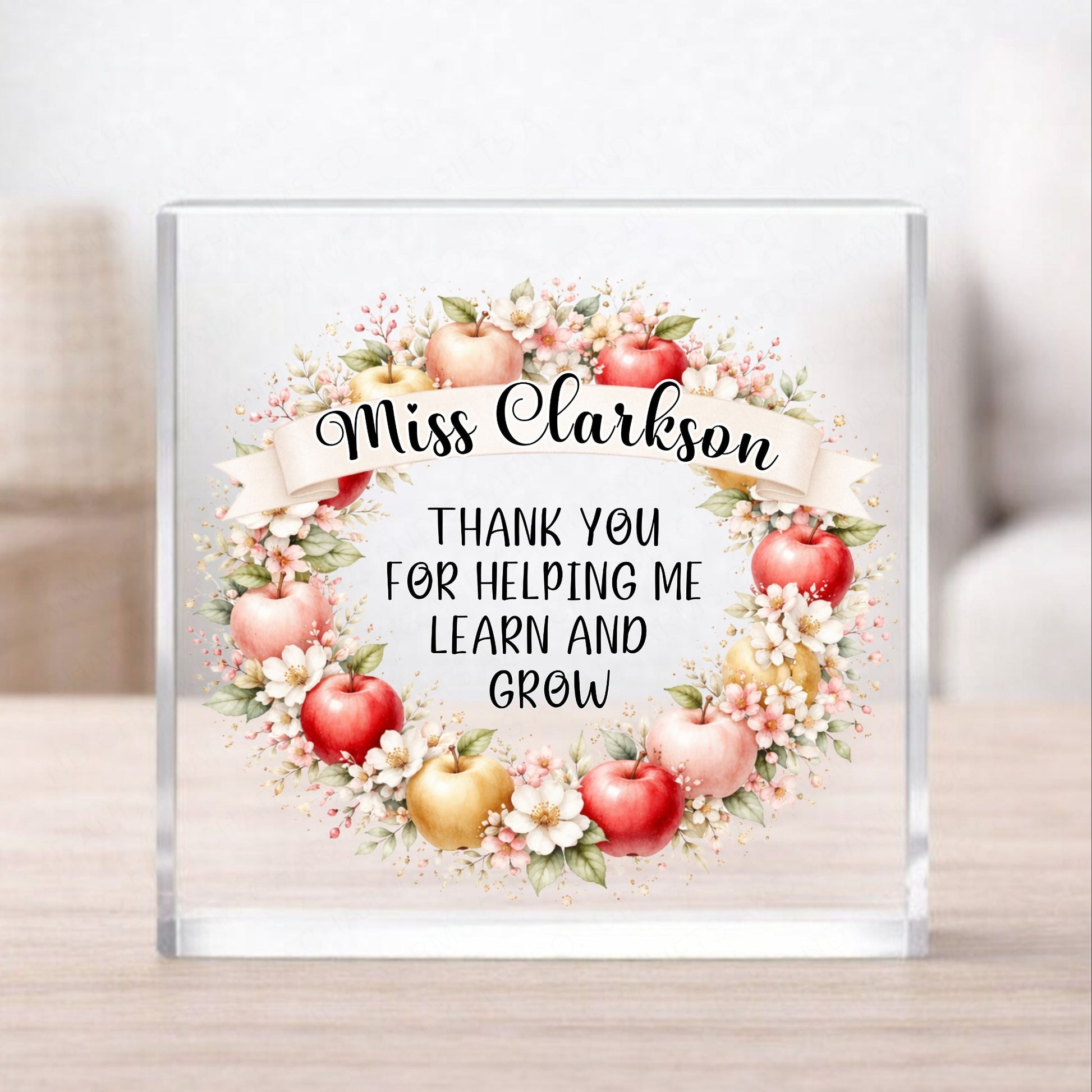 Glass block with floral design and text 'Miss Clarkson Thank you for helping me learn and grow' on a wooden surface.