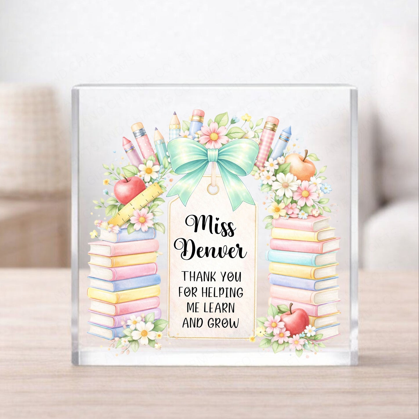Personalized teacher appreciation gift with books, apples, and a bow on a glass block.