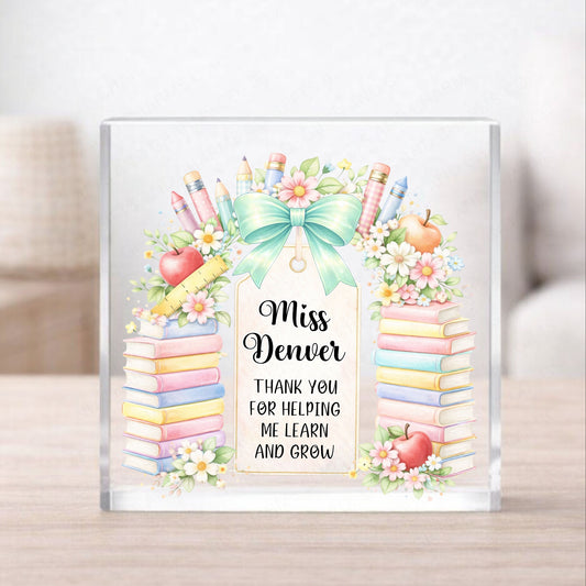 Personalized teacher appreciation gift with books, apples, and a bow on a glass block.