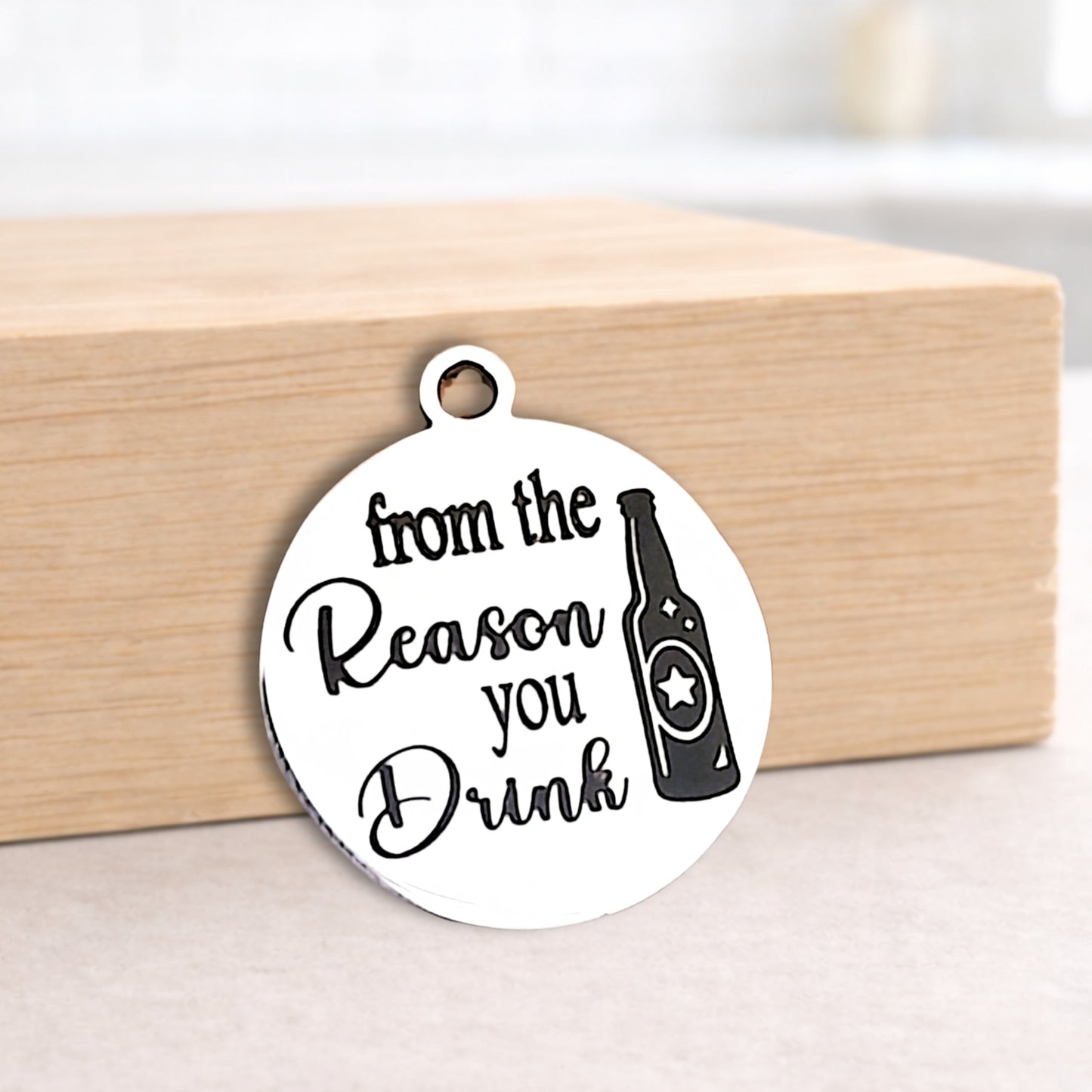 Round metal pendant with text and bottle icon on a wooden block