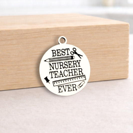 Round metal pendant with 'Best Nursery Teacher Ever' text on a wooden block.