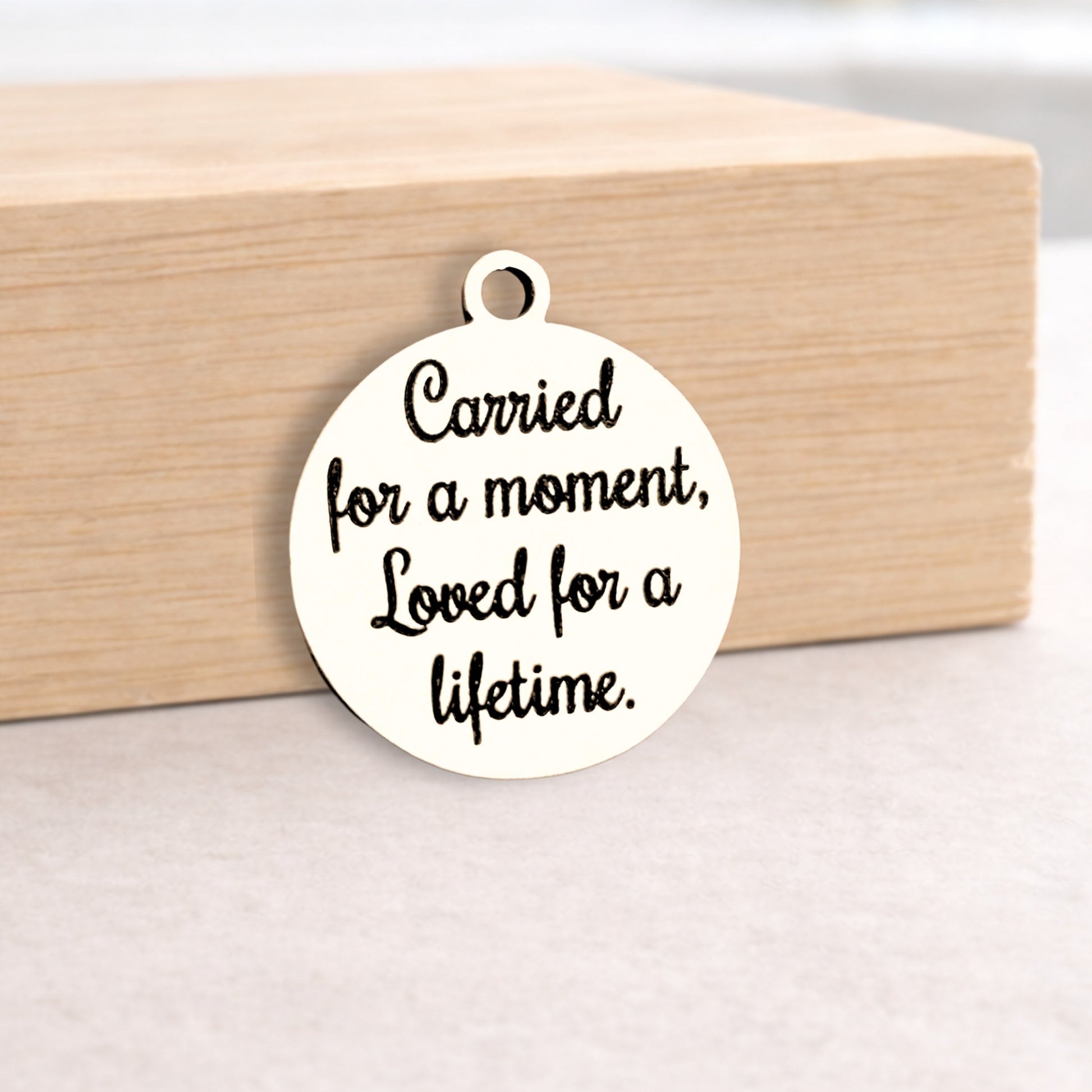 Round metal pendant with engraved text on a wooden block