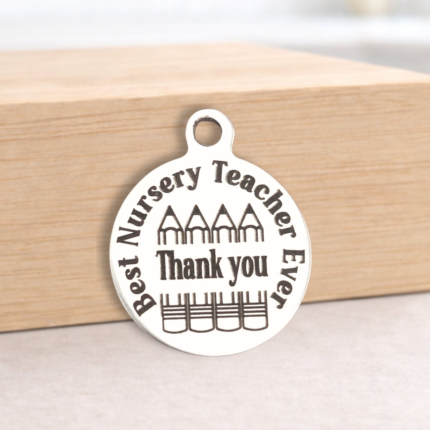 Silver pendant with 'Best Nursery Teacher Ever Thank you' text on a wooden block.