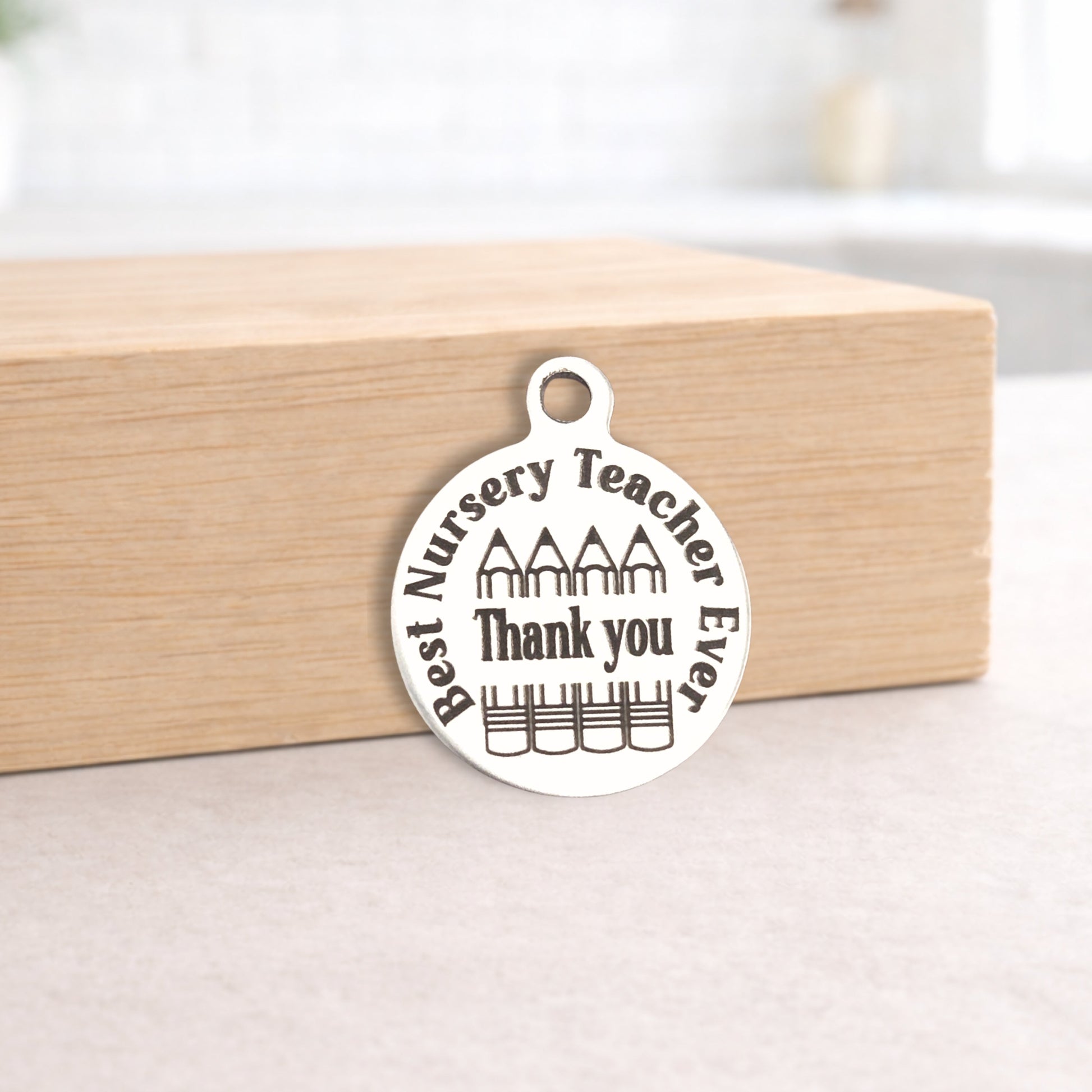 Silver pendant with 'Best Nursery Teacher Ever Thank you' text on a wooden block.