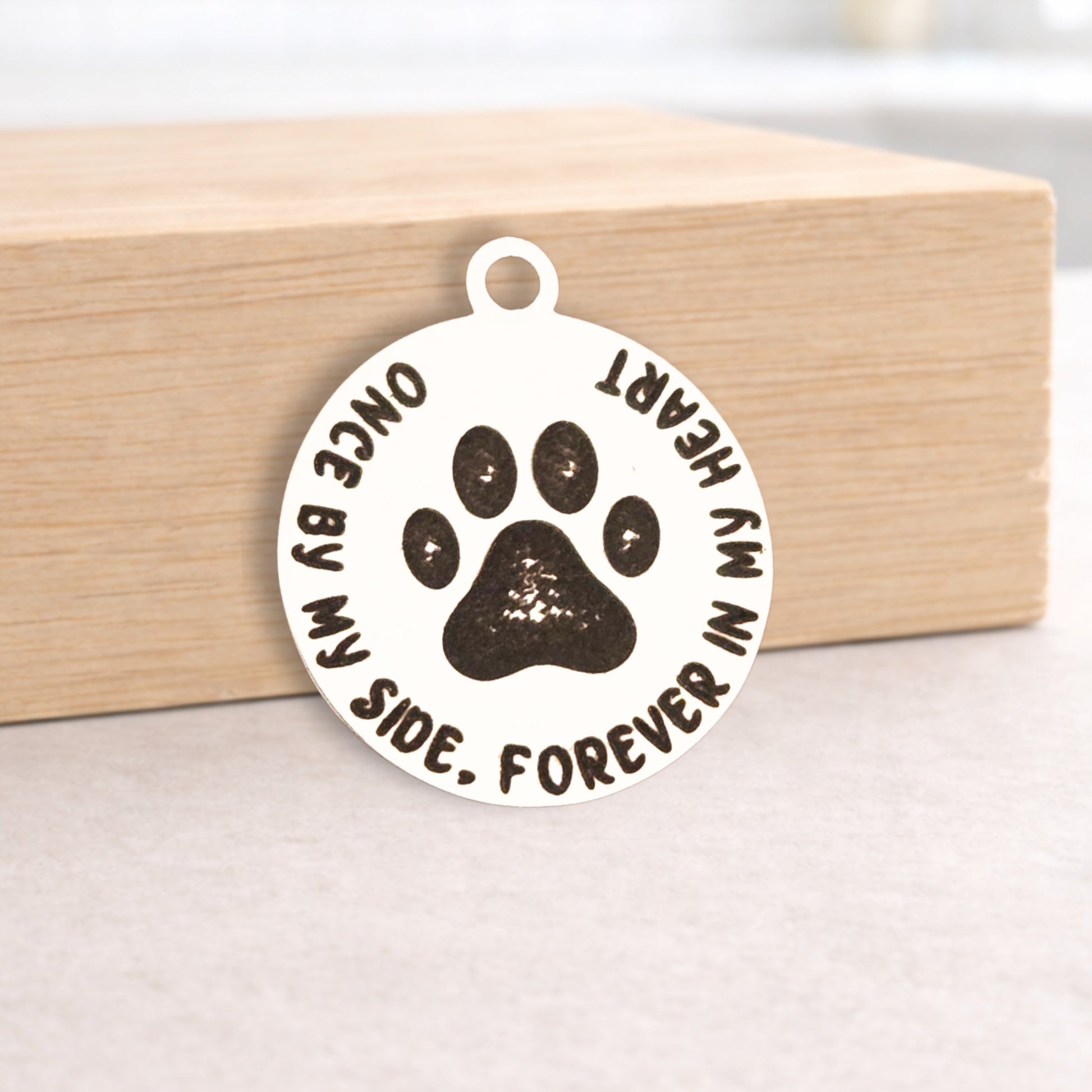 Pendant with paw print and text 'Once by my side, forever in my heart' on a wooden block.