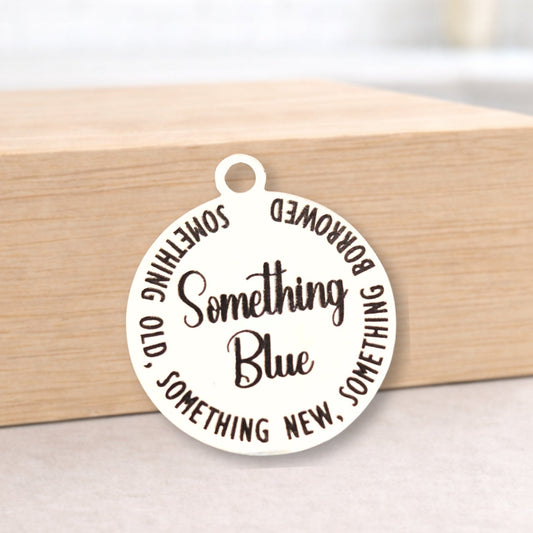 Round metal pendant with 'Something Blue' engraving on a wooden box.