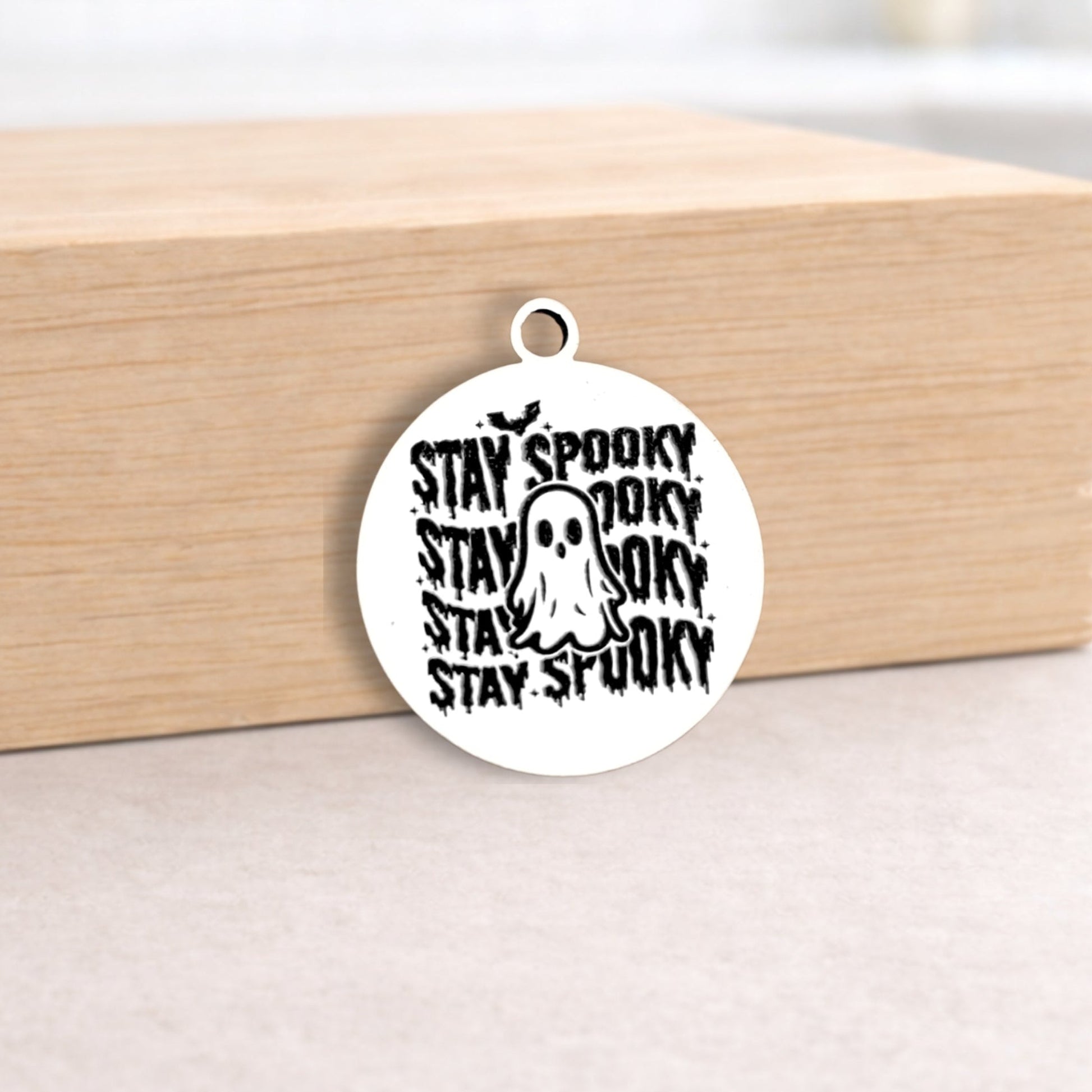 Circular pendant with 'Stay Spooky' text and ghost graphic on a wooden block.