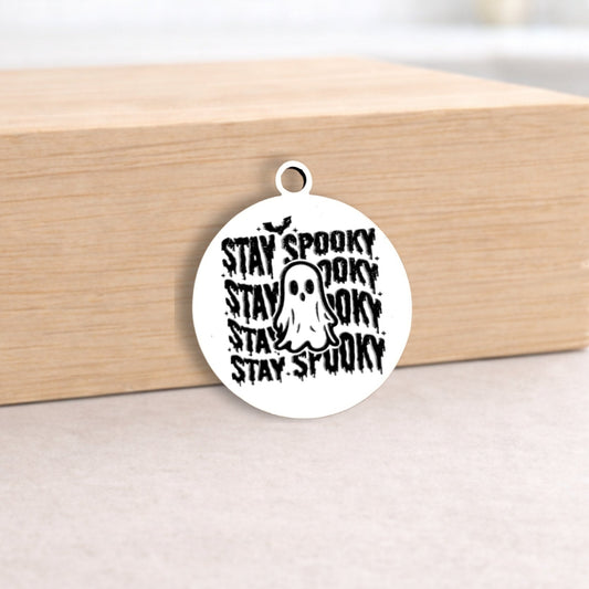 Circular pendant with 'Stay Spooky' text and ghost graphic on a wooden block.