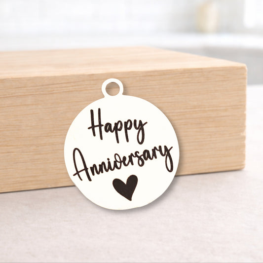 Round white pendant with 'Happy Anniversary' text and heart symbol on a wooden block.