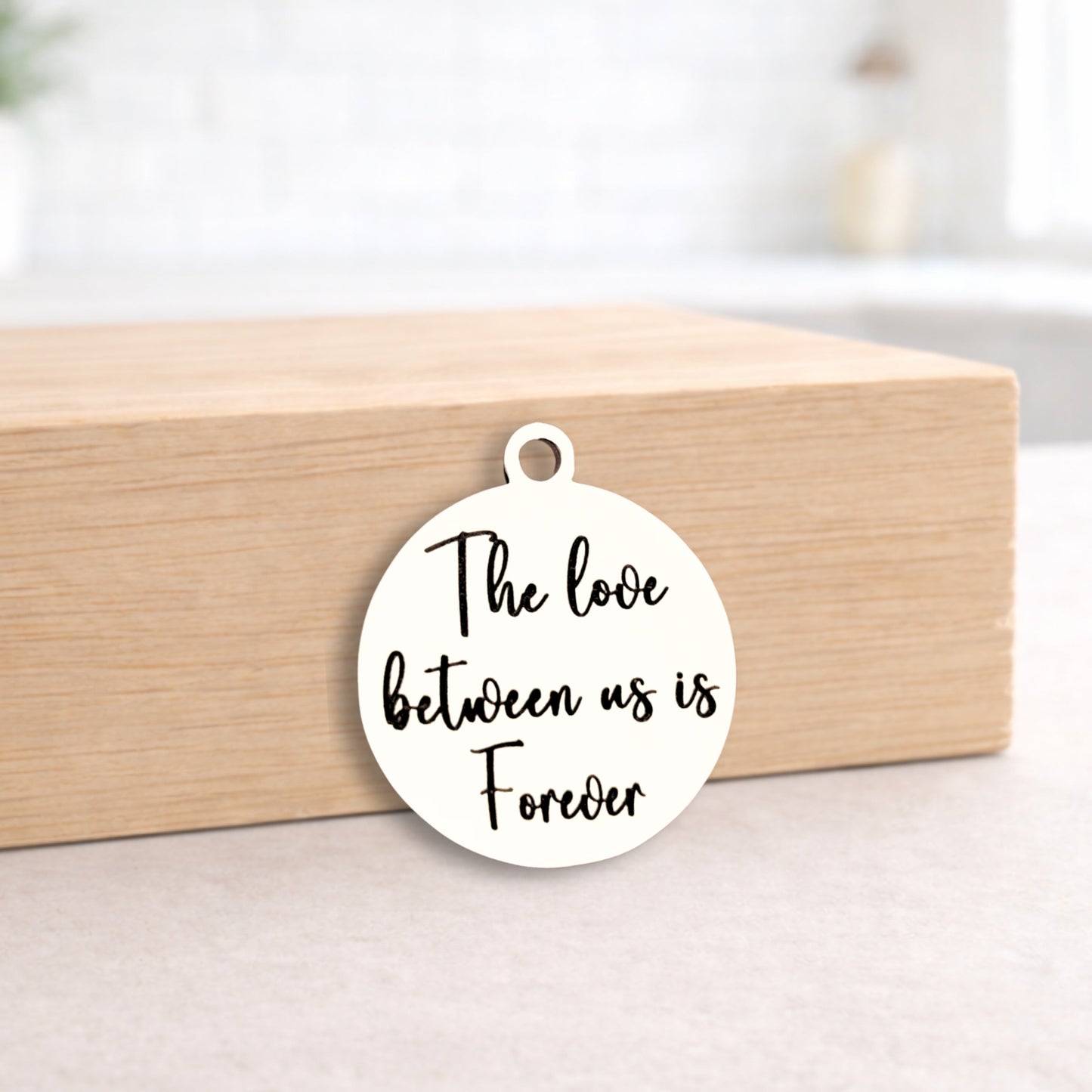 Round white pendant with 'The love between us is Forever' text on a wooden block.