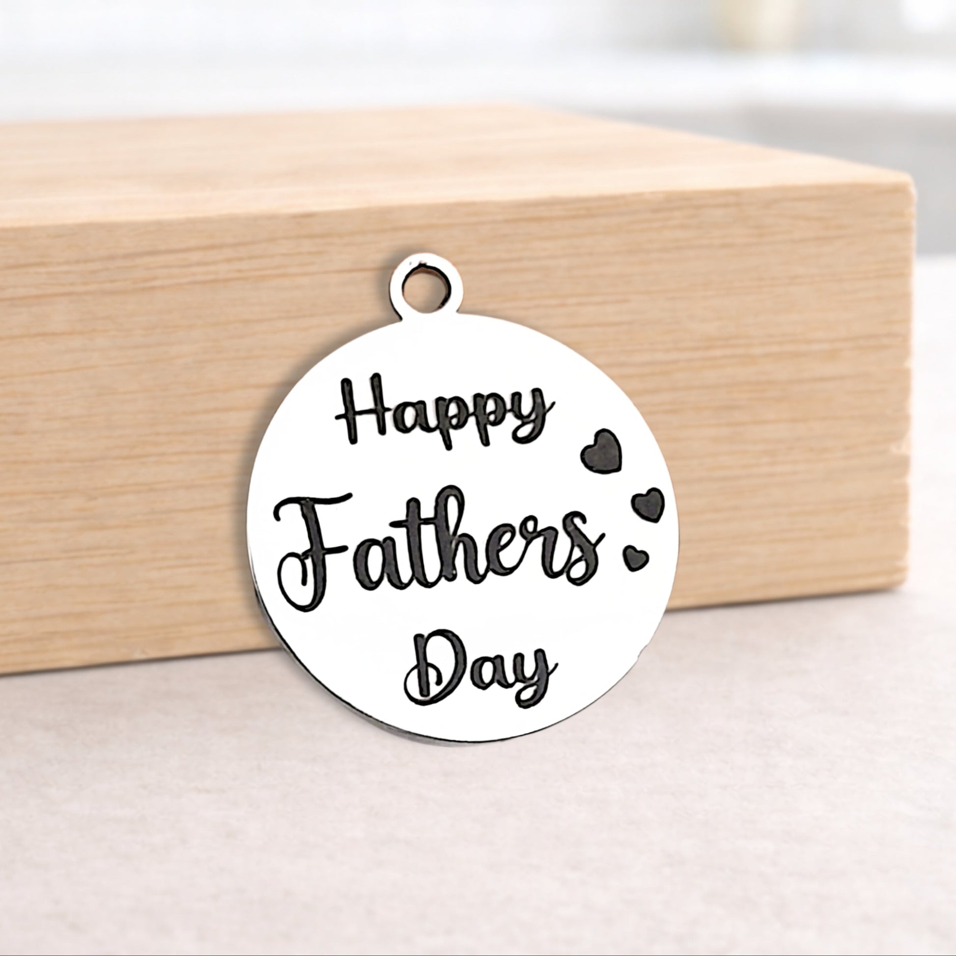 Round metal pendant with 'Happy Fathers Day' text on a wooden block