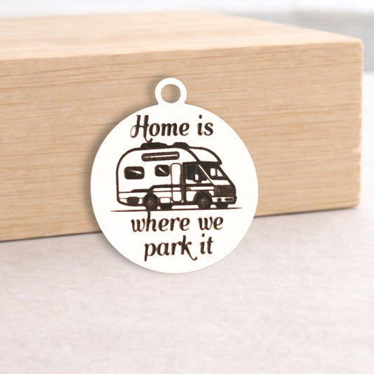 Circular metal pendant with 'Home is where we park it' text and RV illustration on a wooden block.