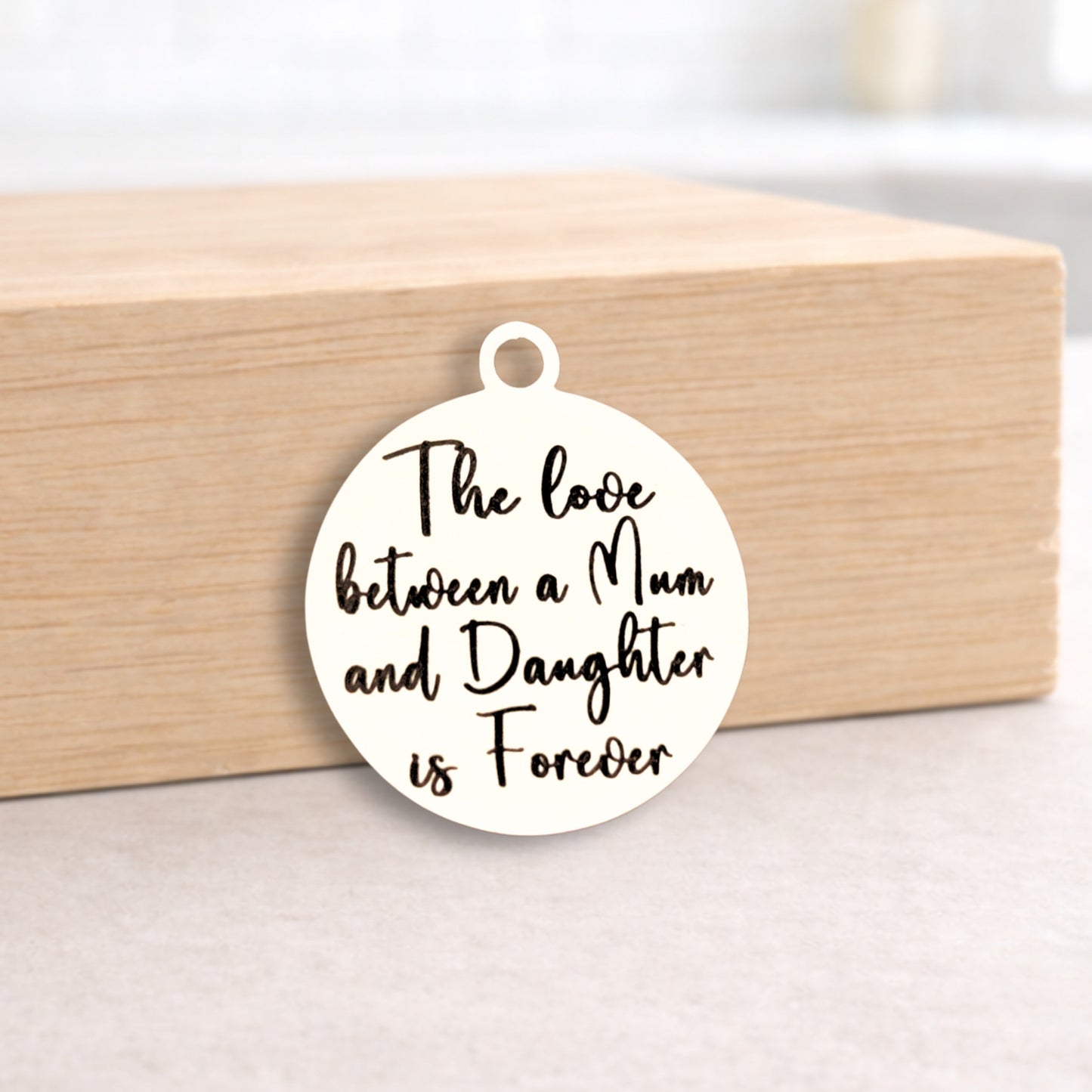 Round pendant with 'The love between a Mum and Daughter is Forever' text on a wooden block.