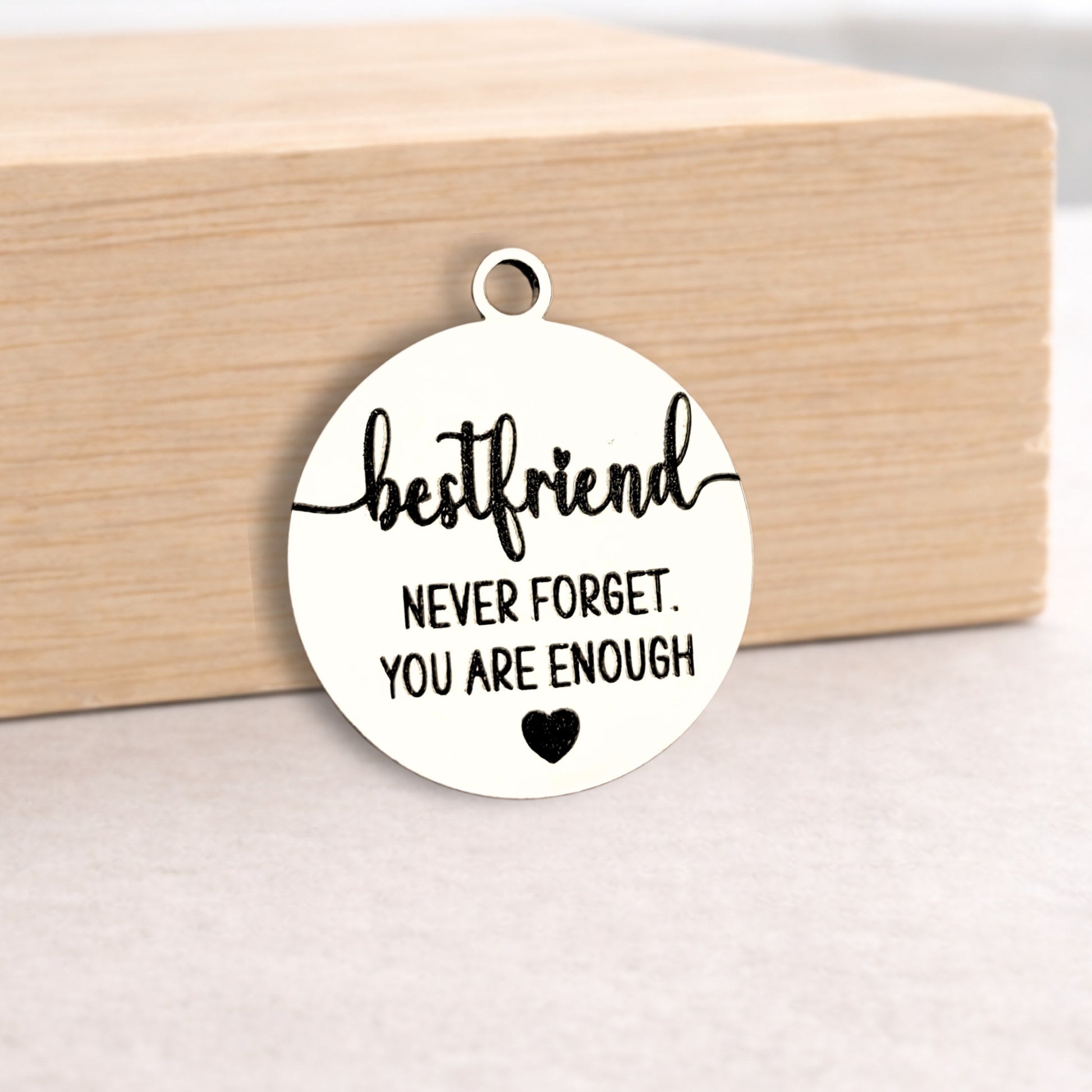 Round metal pendant with 'bestfriend never forget. You are enough' text on a wooden block.