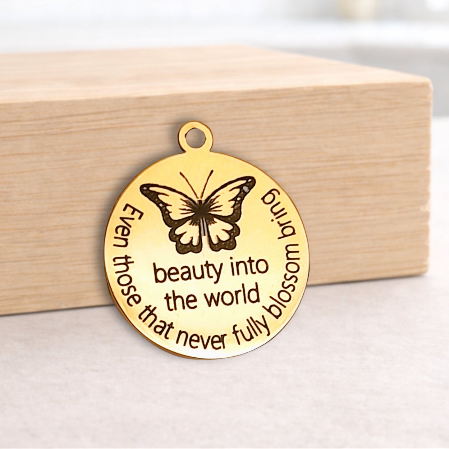 Gold butterfly pendant with engraved text on a wooden block