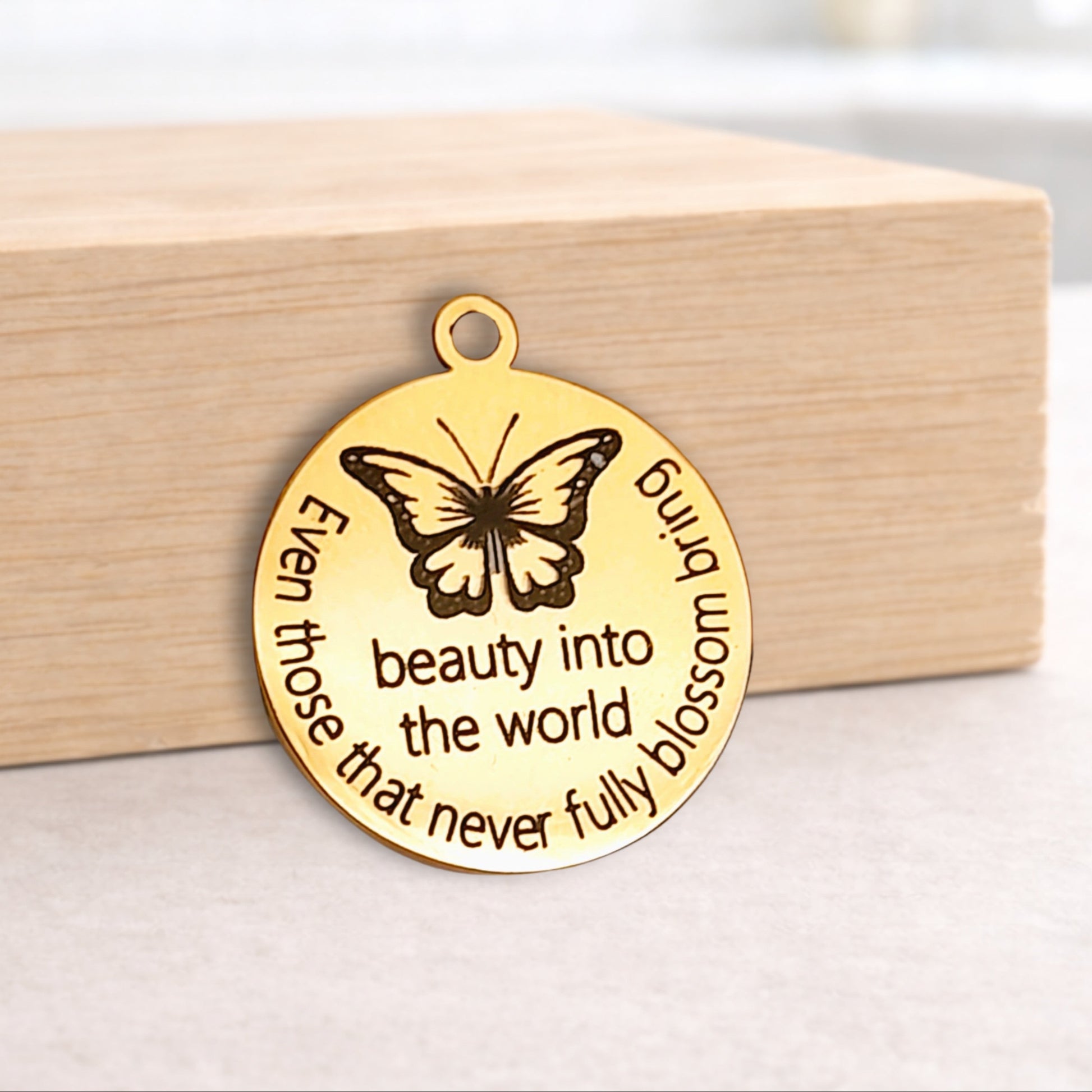 Gold butterfly pendant with engraved text on a wooden block