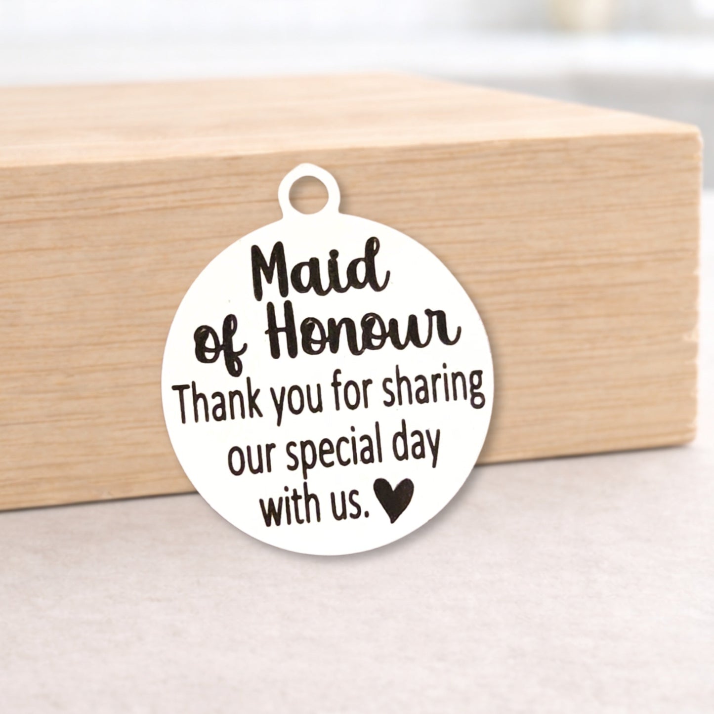 Round metal tag with 'Maid of Honour' text on a wooden block