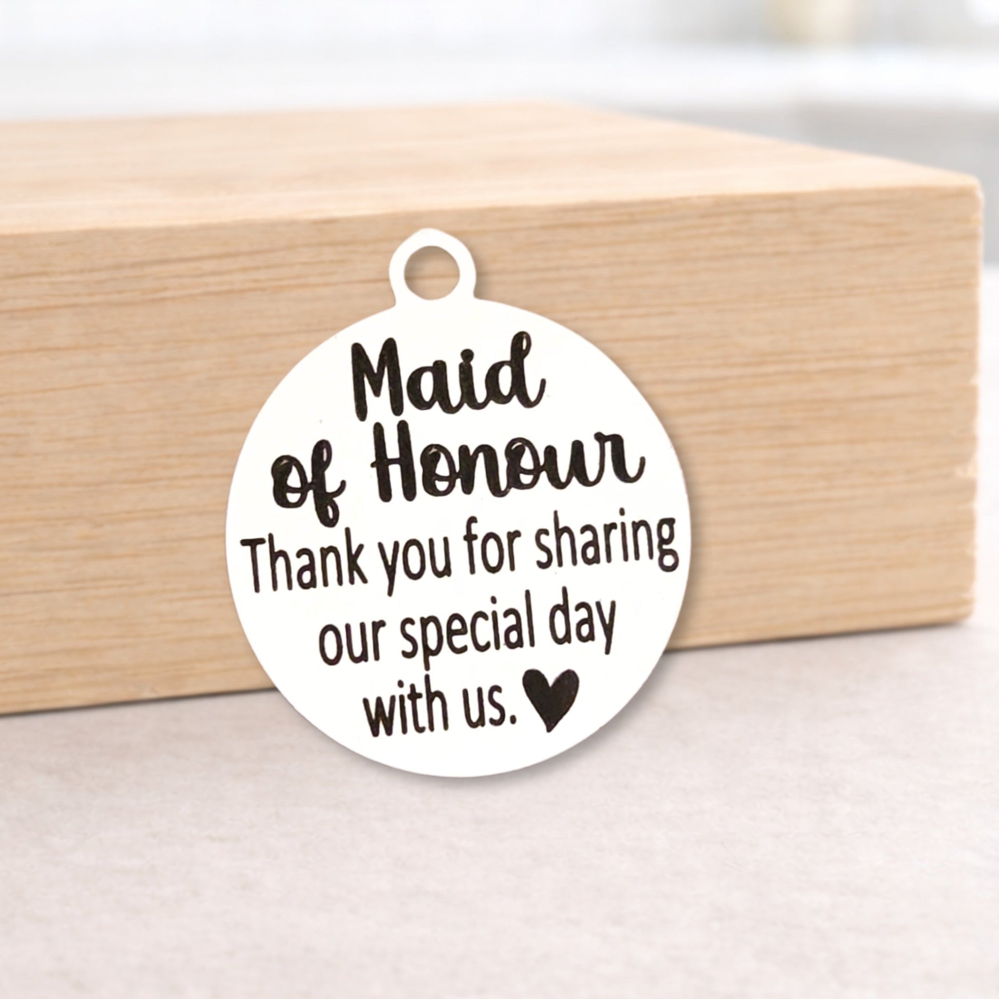 Round metal tag with 'Maid of Honour' text on a wooden block