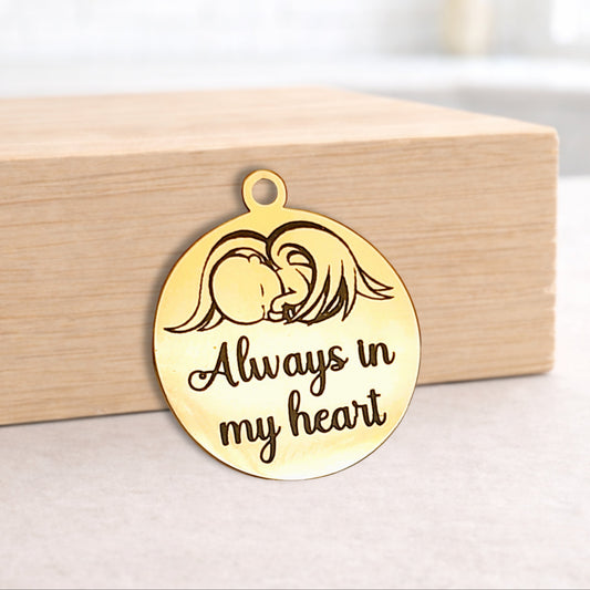 Gold pendant with angel design and 'Always in my heart' text on a wooden block.