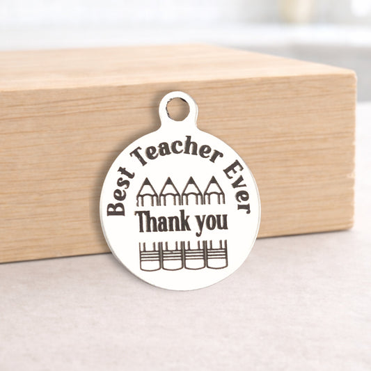Round metal pendant with 'Best Teacher Ever Thank you' text on a wooden block.