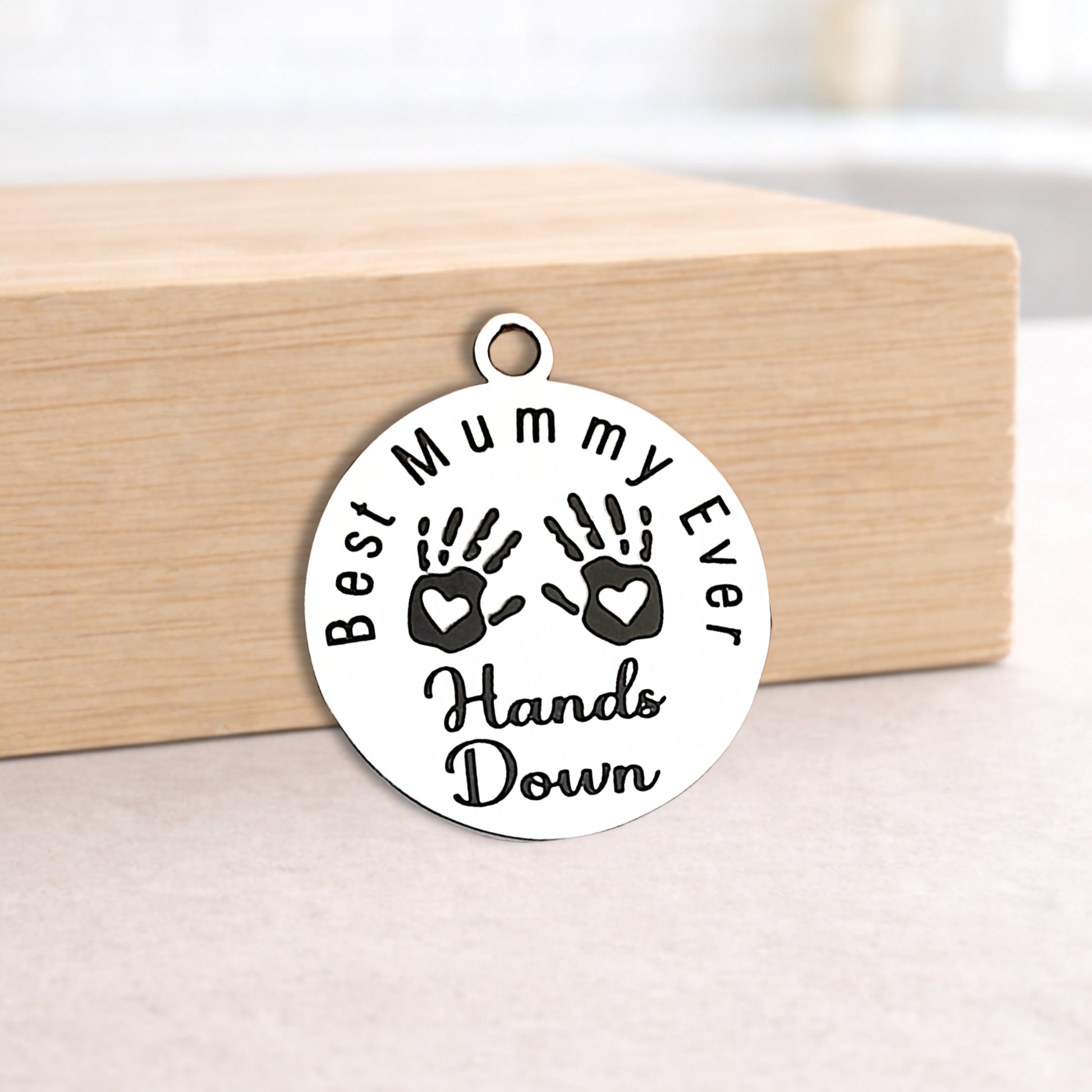 Round silver pendant with 'Best Mummy Ever Hands Down' text and handprints on a wooden block.