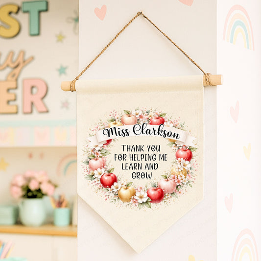 Decorative banner with floral Apple design and text, hanging against a colorful classroom background.