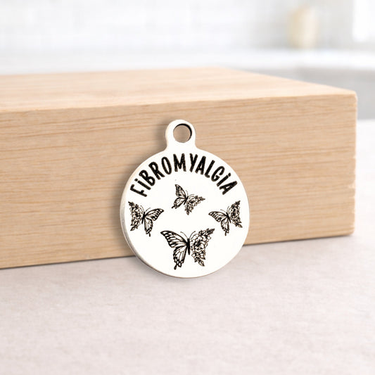 Silver pendant with 'FIBROMYALGIA' and butterfly designs on a wooden block.