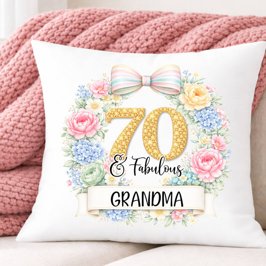 Decorative pillow with floral design and text '70 & Fabulous Grandma' on a pink blanket background.
