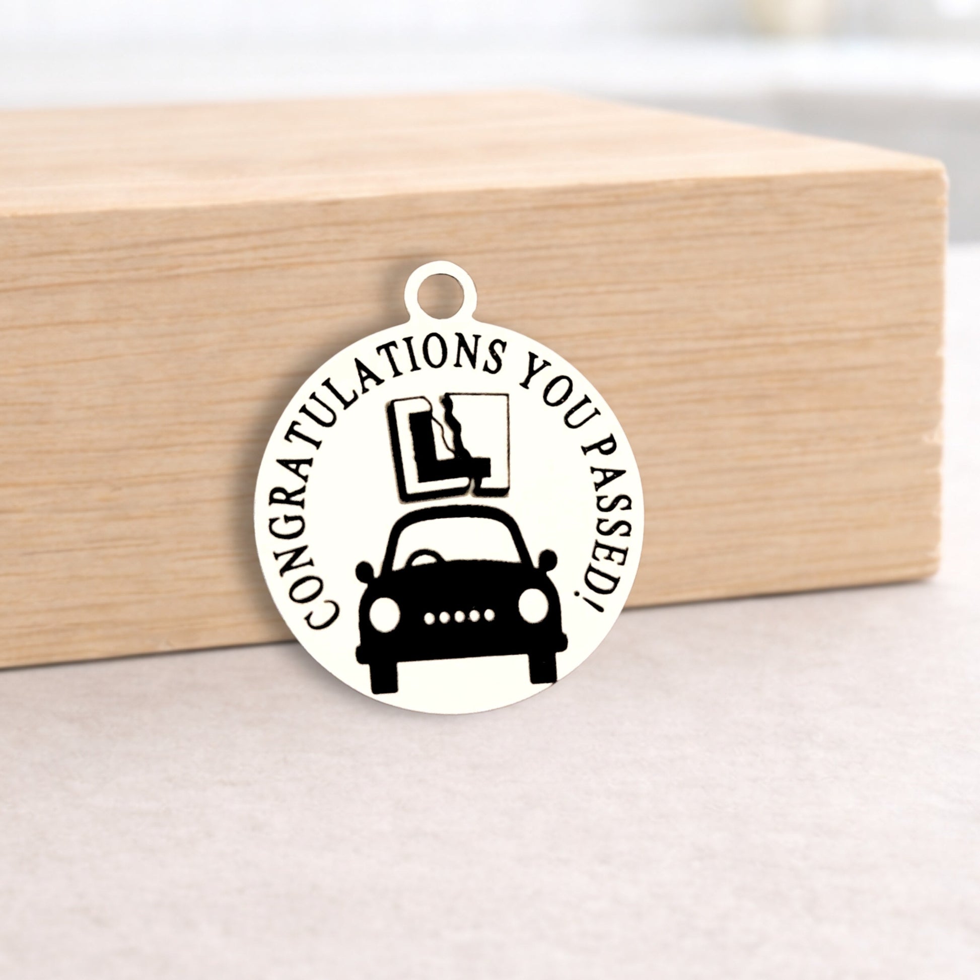 Round metal charm with car and text 'Congratulations you passed!' on a wooden block.