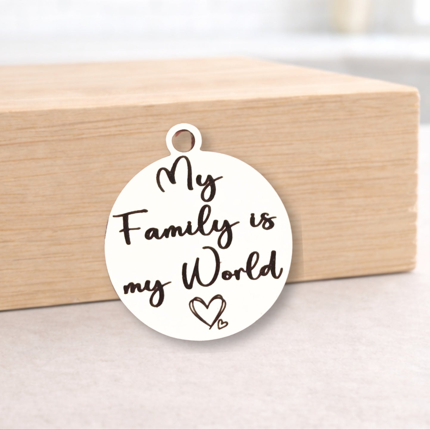 Round metal pendant with 'My Family is my World' text on a wooden block.
