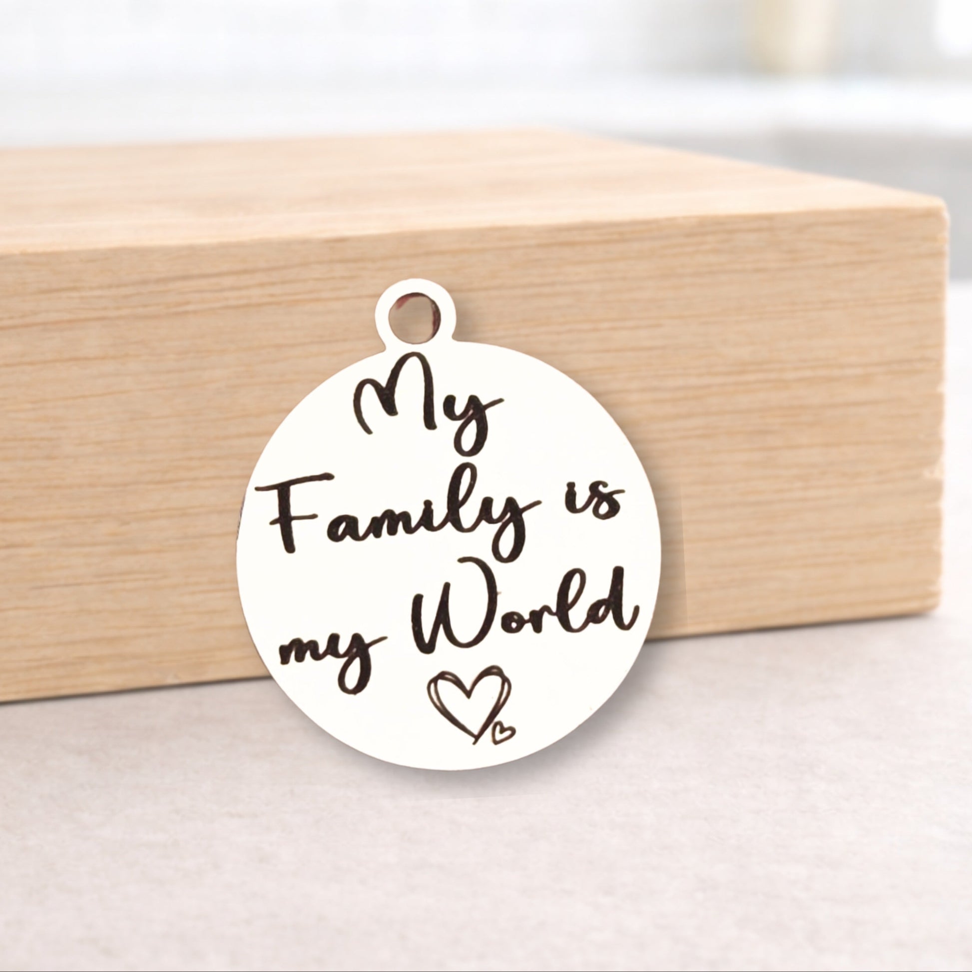 Round metal pendant with 'My Family is my World' text on a wooden block.