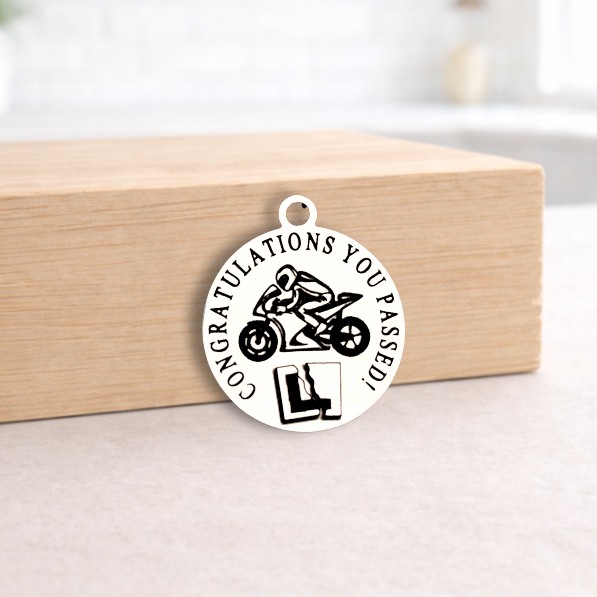 Circular pendant with motorcycle design and 'Congratulations you passed!' text on a wooden block.