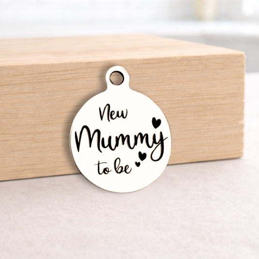 Round white pendant with 'New Mummy to be' text on a wooden block.