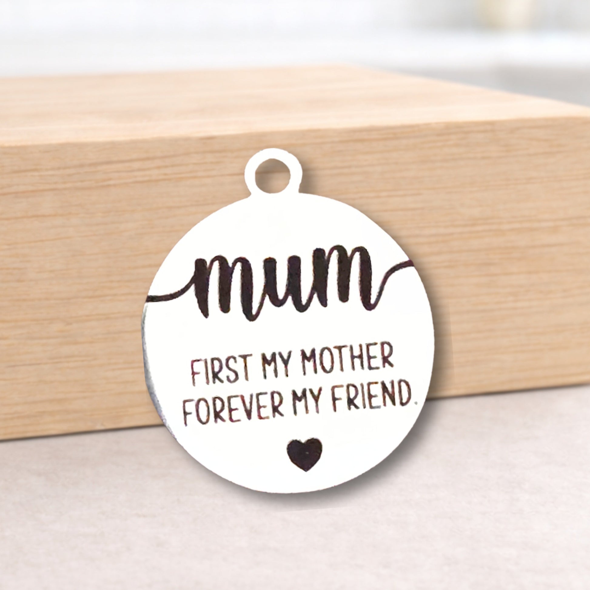Round pendant with 'mum first my mother forever my friend' text on a wooden block.